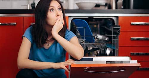 Image: a woman sits next to her broken dishwasher.