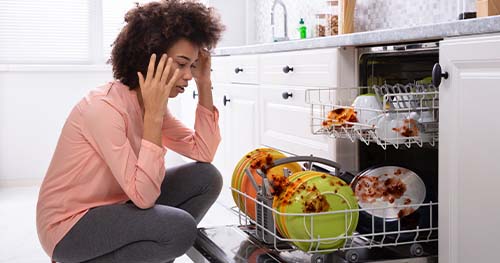 Image: a woman looking at her dirty dishes.