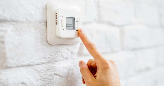 Image: a finger adjusting thermostat settings. When you run heat and ac at the same time, you can use a thermostat to do so effectively.