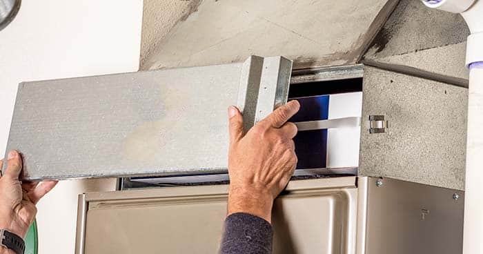 Image: a person changing an air filter as part of regular HVAC maintenance.