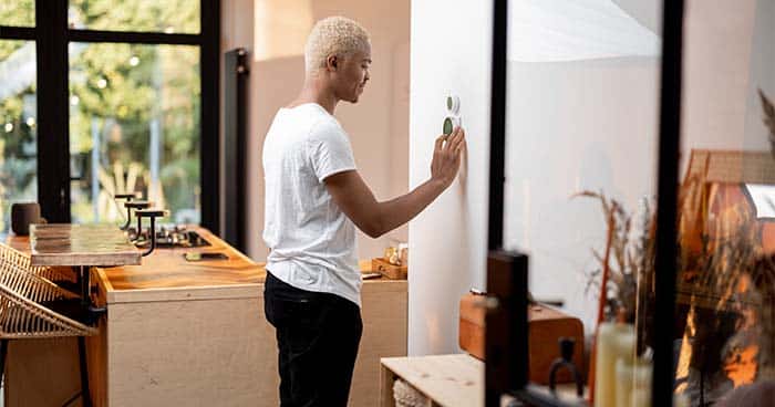 Image: a man adjusting a thermostat.