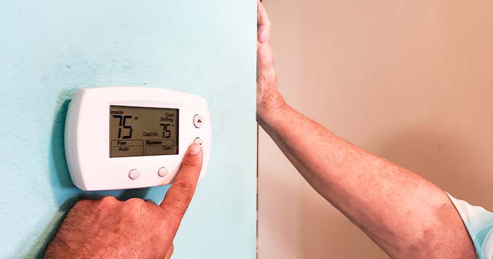 Image: a hand adjusting an older thermostat.