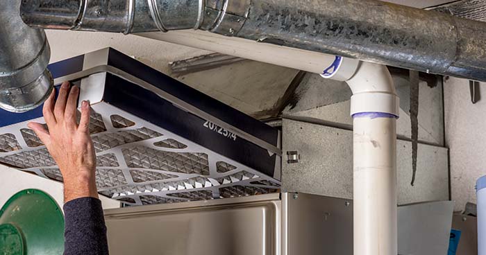Image: a person changing an air filter as part of professional furnace maintenance.