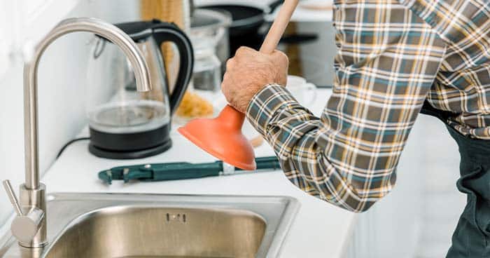 Image: a man plunging a sink with a cup plunger.