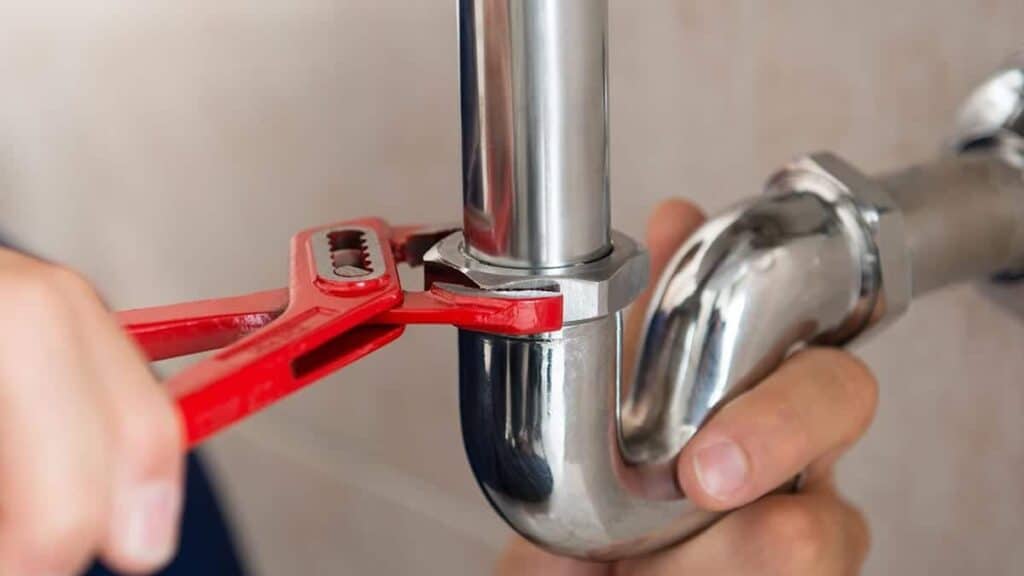 An Adeedo plumber’s hands use a red pipe wrench to expertly tighten a metal pipe beneath a customer’s sink.