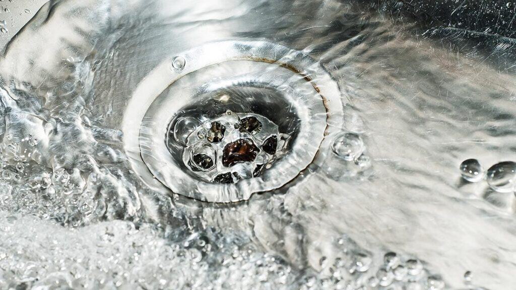 Water drains smoothly down a stainless steel sink, forming bubbles and ripples—a clean result from Adeedo’s expert plumbing service.
