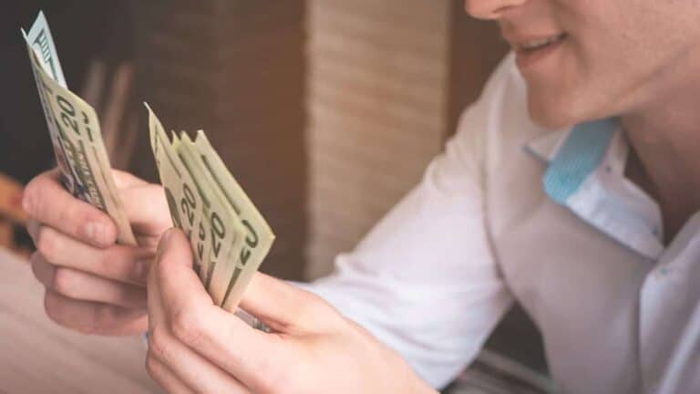 An Adeedo team member in a white shirt counts a stack of twenty-dollar bills, assisting with payment or billing services.