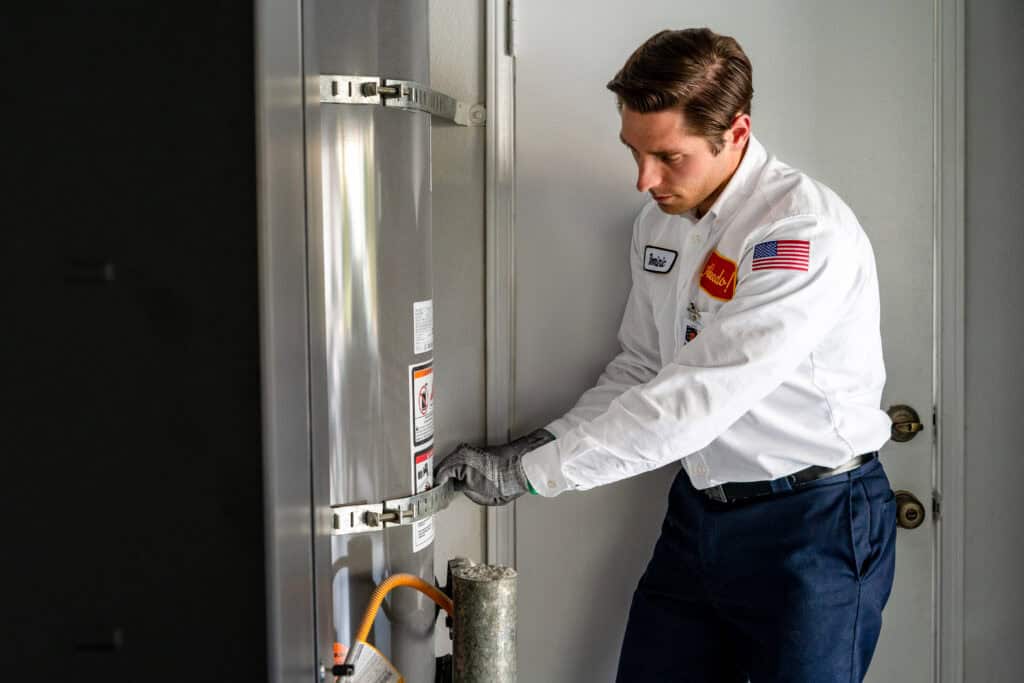 An Adeedo technician in uniform carefully adjusts a water heater in a tidy utility room, wearing gloves for safety while standing next to the door, demonstrating our commitment to professional service.